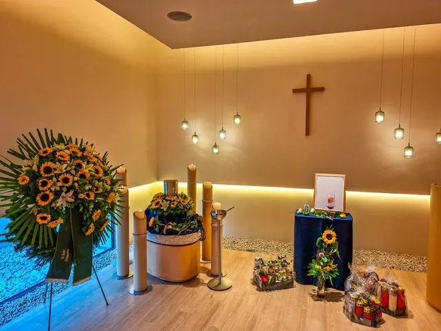 Moderne Aufbahrung mit Silberurne, Sonnenblumen und Holzkreuz in einer Kapelle