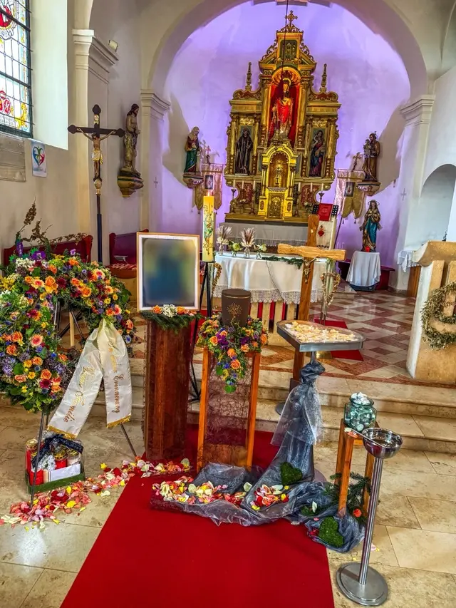 Würdevolle Aufbahrung mit Urne, Blumengesteck und Rosenblättern vor dem Altar einer Kirche