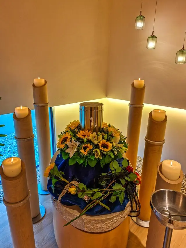 Silberurne mit Sonnenblumen, Lilien und Kerzen bei einer würdevollen Aufbahrung